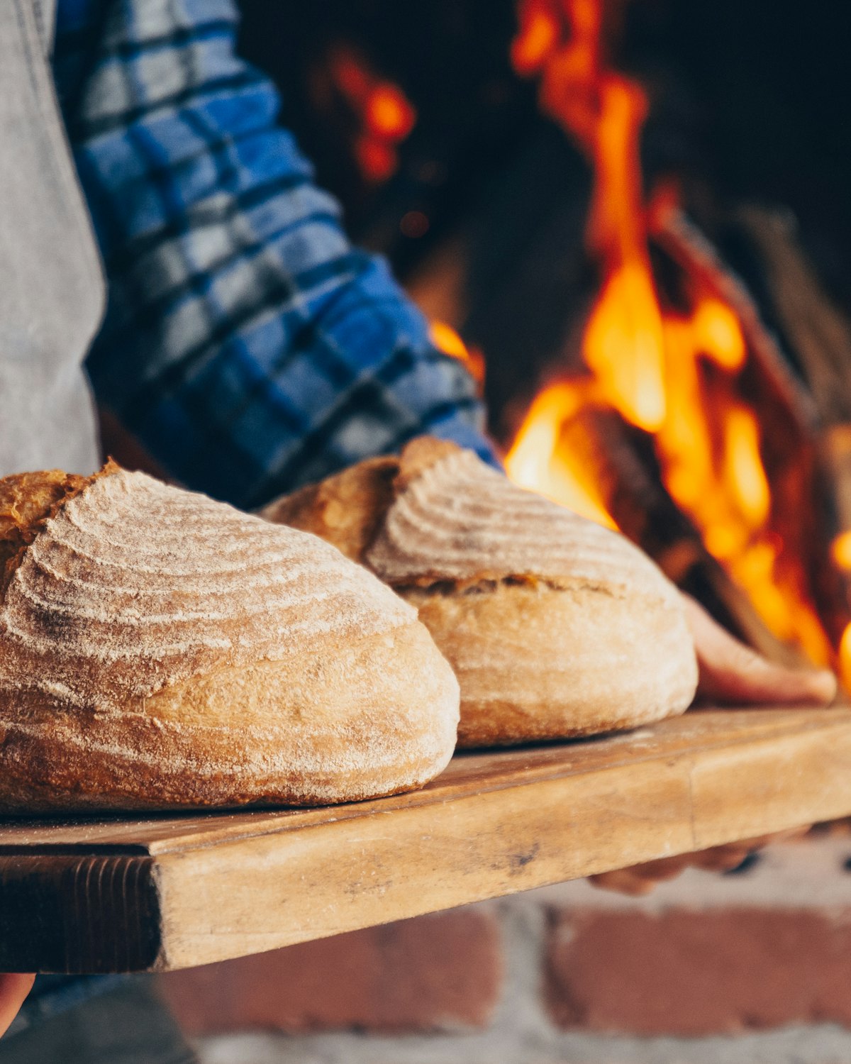 Two country loaves on a wooden peel in front of the open fire.