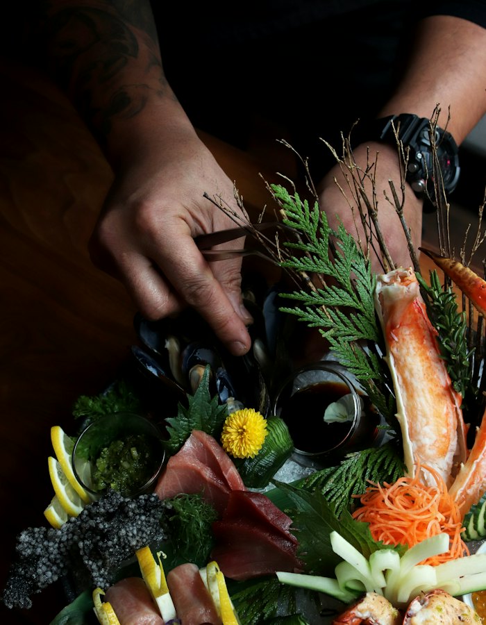 Hands arranging shellfish and cedar on a platter.