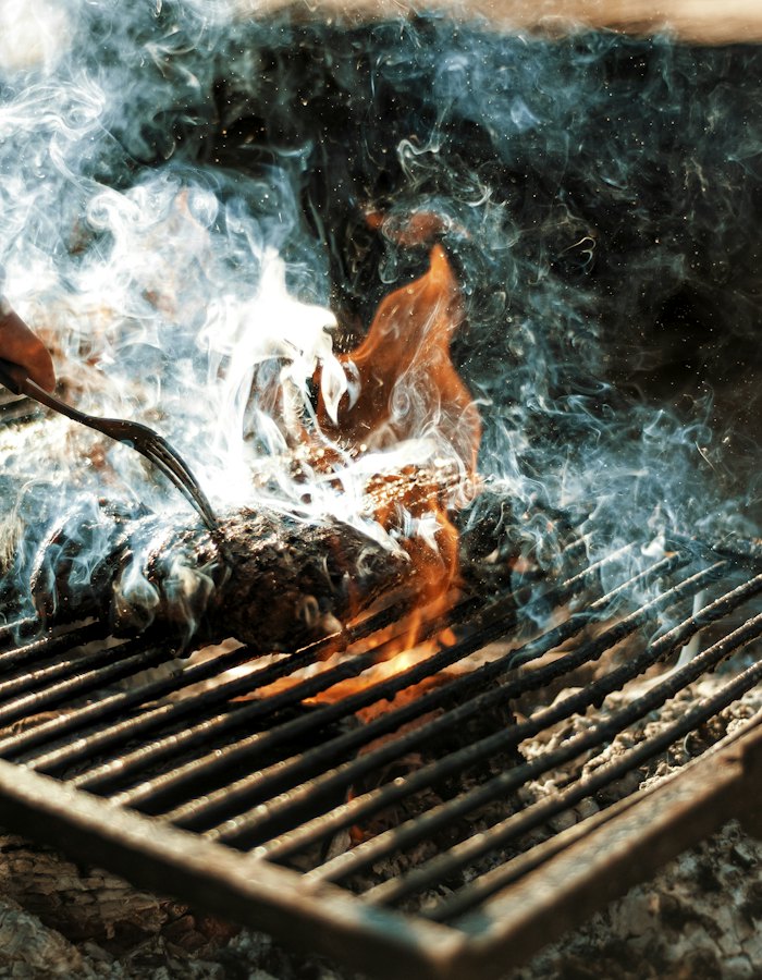 Fish going onto the grill over the coals, smoke rising.