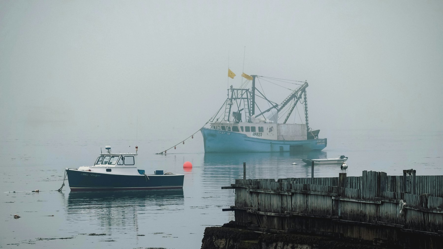 A trawler and a small skiff sitting in fog beside the old pier pilings.