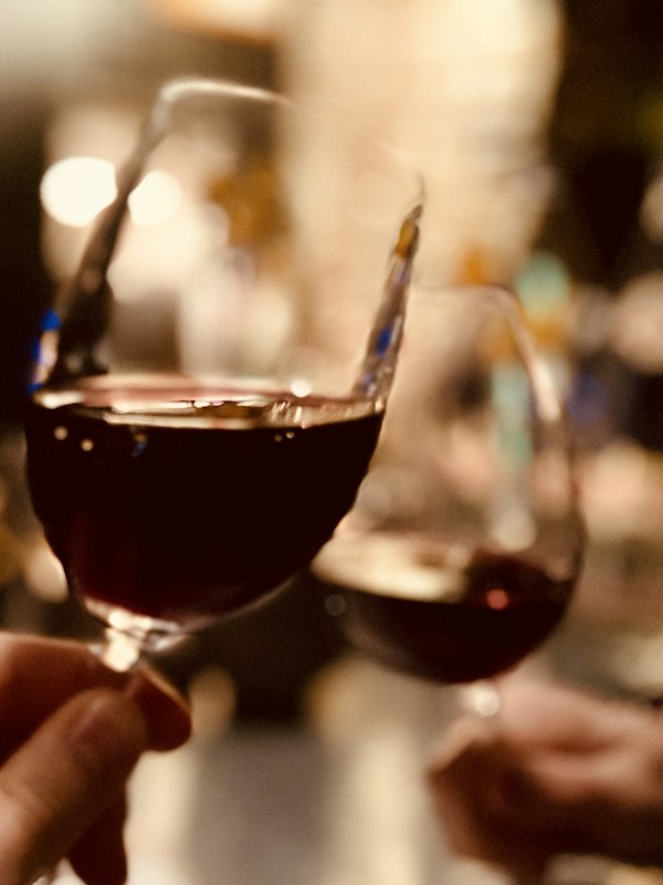 Two glasses of red wine meeting across the table, candlelight behind.